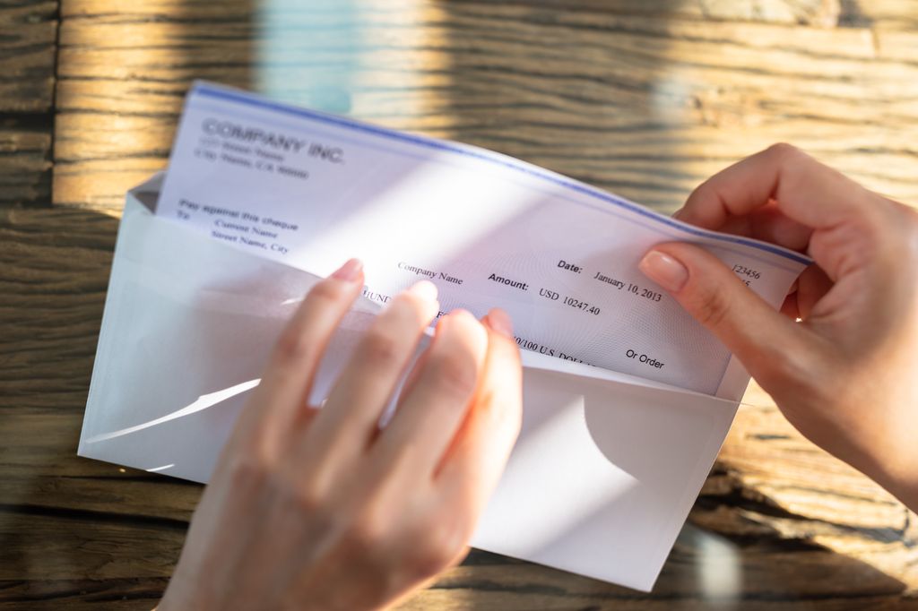 A person opening an envelope containing a paycheck.