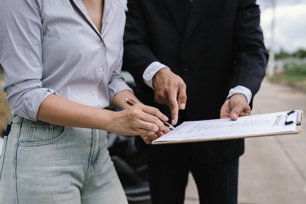 Two people are reviewing and signing a document on a clipboard outdoors.